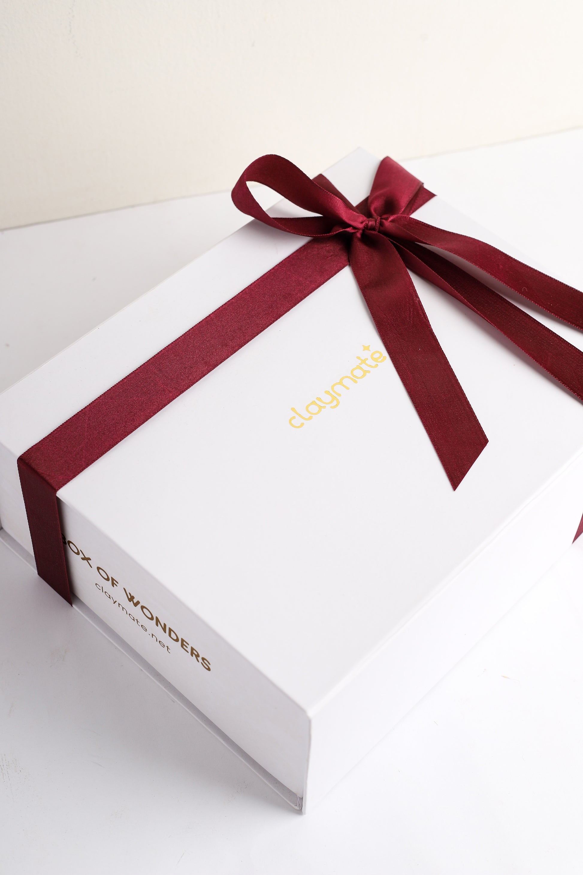 A white magnetic gift box with a maroon ribbon and bow on top. The brand 'Claymate' is visible on the box.