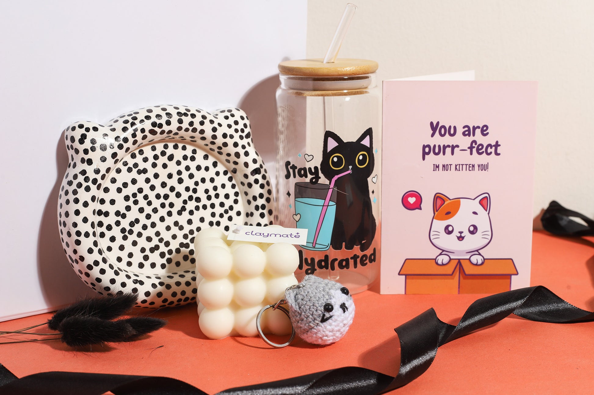 Cute cat-themed gift box featuring a ‘You are purr-fect’ greeting card, cat crochet keychain, bubble candle, black cat hydration tumbler, and polka dot ceramic dish on an orange background.