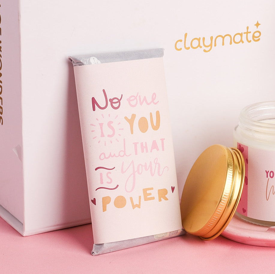 Gift box with candle, notebook, and other items on a pink surface.