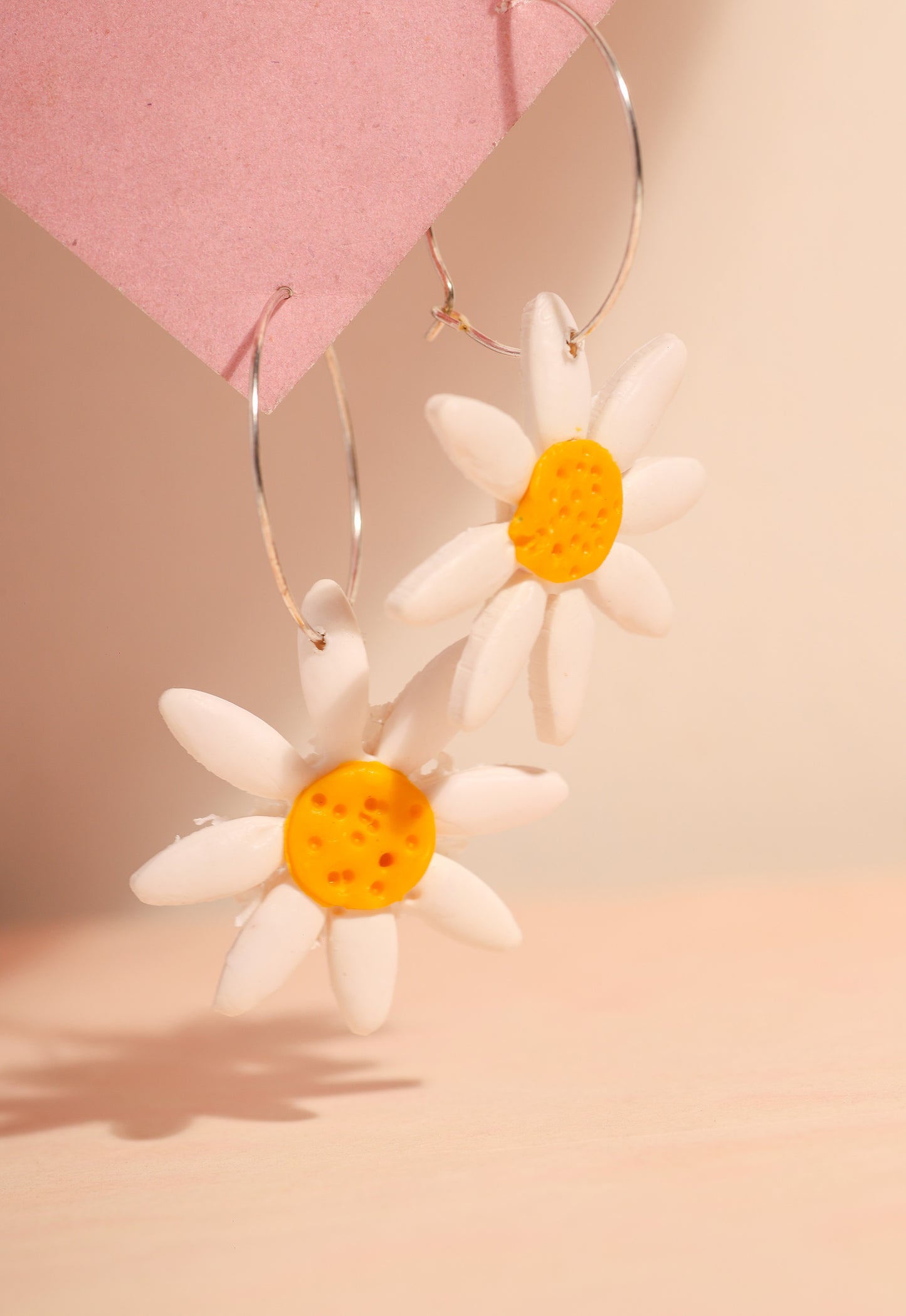 Daisy hoop earrings on a pink background