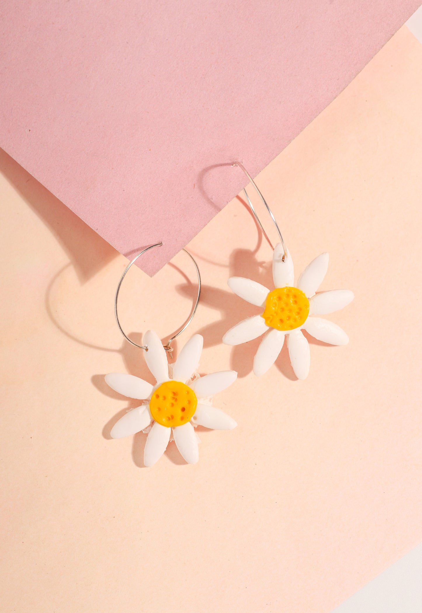 Daisy hoop earrings on a pink background