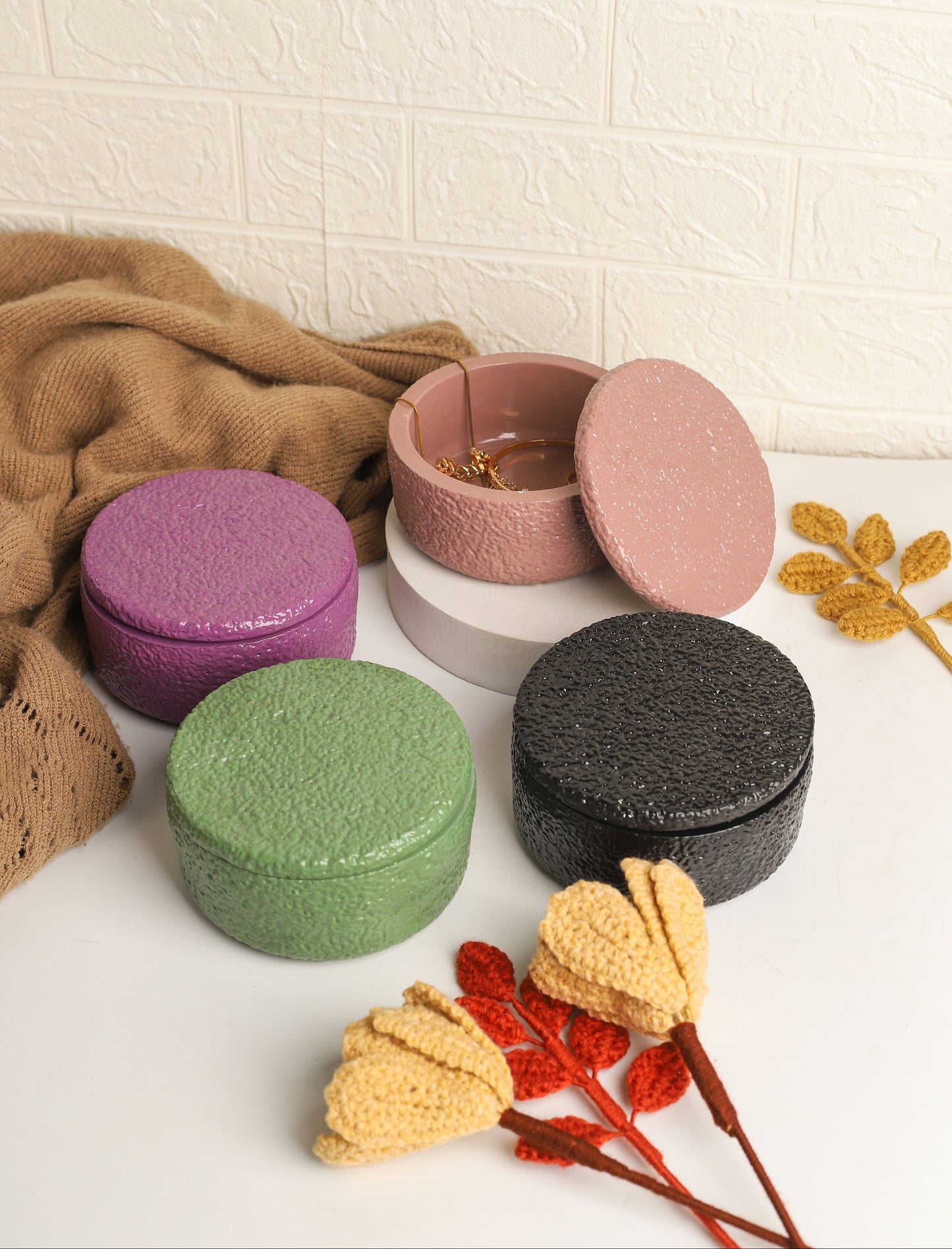 Set of colorful round containers on a textured white surface with decorative leaves.